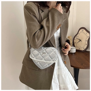 Detail of silver heart-shaped quilted bag with pearl bow charm and chain strap
