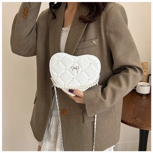 Detail of white heart-shaped quilted bag with metal bow and pearl fringe trim