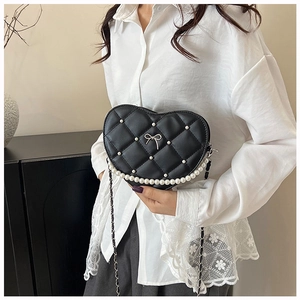 Close-up of heart-shaped quilted bag with pearl accents and bow detail on a model