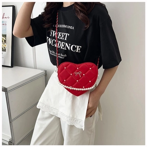 Detail of red heart-shaped quilted bag with pearls and metal bow on a model