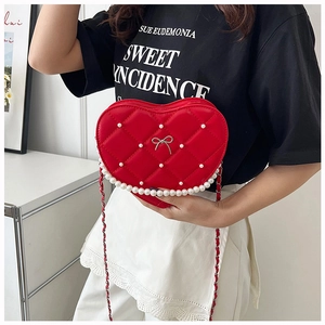 Red heart-shaped quilted crossbody bag with pearl accents and silver bow on model