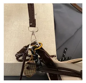 Detail of leather strap with silver hook and gold tennis racket charm on tote bag