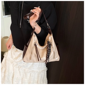 Detail of a color-block tote bag with dual zippers and long leather tassels on cream patent leather