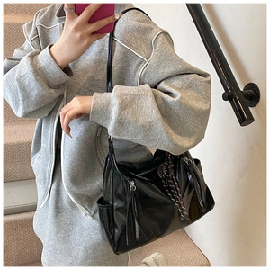 Detail of a black patent leather tote bag with glossy finish and sleek side zipper