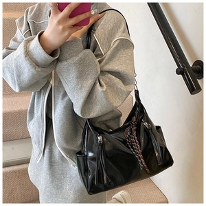 Detail of a black glossy shoulder bag with double zippers and a striped silk scarf detail