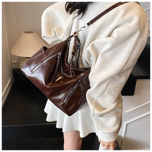 Detail view of dark brown glossy patent leather crossbody bag with silver zipper accents