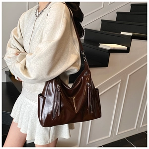 Detail of glossy brown tote bag featuring side fringe zippers and textured leather finish