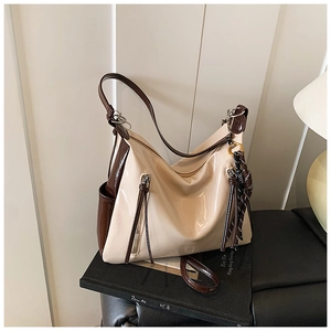 Detail of hobo bag in cream and brown patent leather featuring decorative zippers