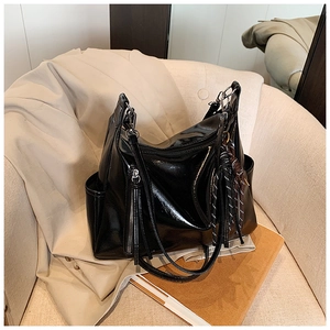 Detail of black glossy leather hobo bag featuring side zip and woven tassel pendant
