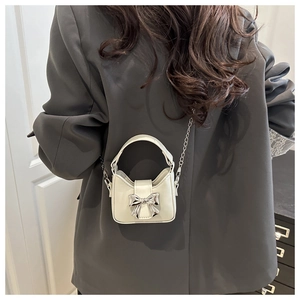 Detail der cremeweißen Mini-Tasche mit silberner Schleife auf grauem Sakko am Model