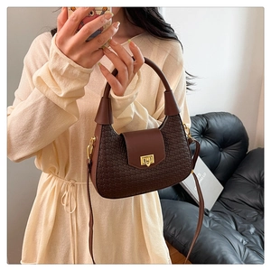 Detail of dark brown crescent bag with woven texture and gold twist lock on sofa