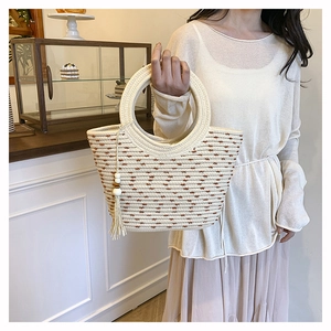 Détail du sac seau en paille tressée avec pois marrons et pompon ethnique en bois