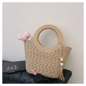 Dettaglio borsa tote in paglia intrecciata con manici rotondi e nappa decorativa in legno