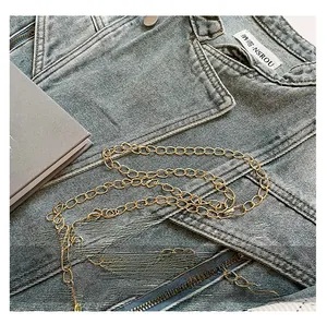 Close-up of a glossy gold metal chain strap on light blue denim jacket with book detail