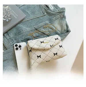 Close-up of beige corduroy crossbody bag with black bow embroidery and golden chain