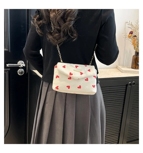 Close-up of white corduroy crossbody bag featuring red heart patterns and gold chain
