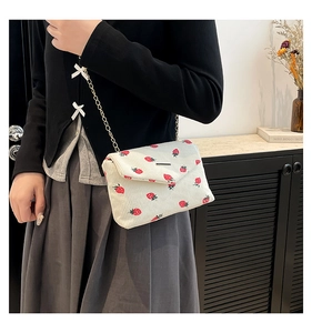Detailed shot of white corduroy mini bag with red strawberry print and gold chain strap