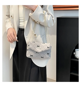 Detail of quilted crossbody bag with black bow accents and golden chain strap for women