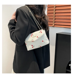 Close-up of beige corduroy shoulder bag featuring red cherry embroidery and gold chain strap