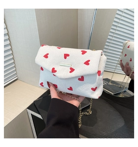 Detail of white corduroy shoulder bag with red hearts and golden chain strap