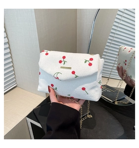 Detailed close-up of a white corduroy crossbody bag with cute cherry embroidery and gold chain