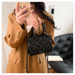Detail of black quilted PU leather handbag featuring woven texture and fashion slogan