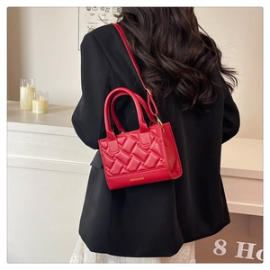 Detail of red quilted faux leather handbag worn with a chic black blazer in a warm room