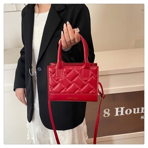 Detail of red quilted PU leather handbag featuring elegant gold text and top handles