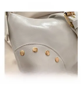 Vue détaillée du cuir blanc avec clous dorés et boucle métallique sur le côté du sac
