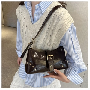 Detail of dark brown glossy underarm bag with gold buckle and rivets worn by model