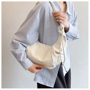 Detail of white half-moon shoulder bag featuring soft pleated leather and knotted strap