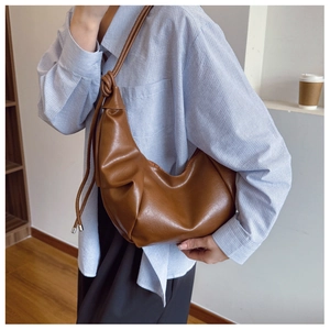 Detail of caramel brown PU leather half-moon bag with soft pleats and knotted strap detail