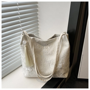 Détail d'un sac cabas en dentelle blanche avec broderie papillon et glands soyeux