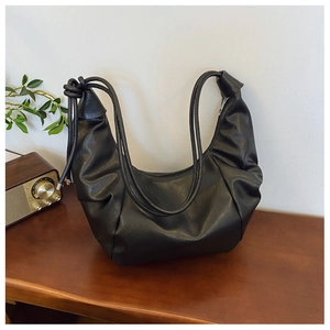 Detail of black dumpling hobo bag with knotted strap on wooden desk for casual styling