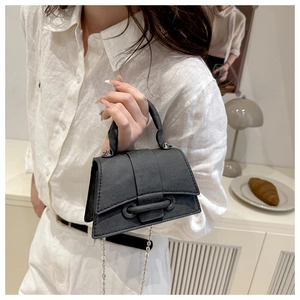 Detail of a black structured mini handbag with a curved base and silver chain strap