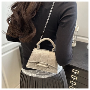 Detail of silver textured crossbody bag with metal chain strap and unique buckle closure