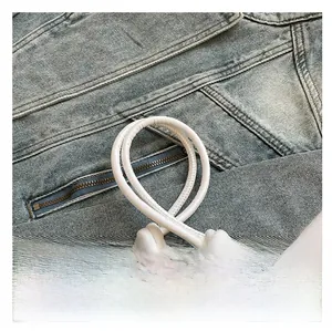 Detail of white leather shoulder strap with elegant knots and metallic hardware on denim
