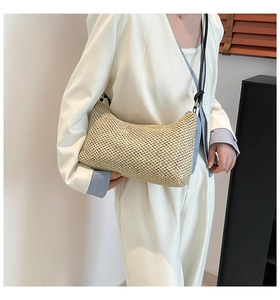 Close-up of woven straw shoulder bag with black leather strap and metal zipper detail