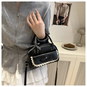 Détail d'un sac noir avec dentelle blanche et ruban à carreaux sur la poignée