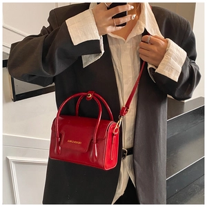 Close-up of a red glossy crossbody bag with gold hardware and FASHION & BAGS text