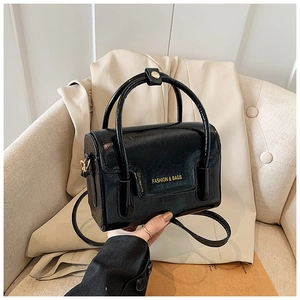 Detail of glossy black mini handbag with gold lettering and hard curved top handle