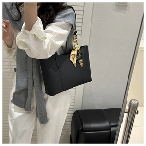 Detail of minimalist black tote bag with elegant patterned silk scarf on shoulder strap