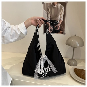 Detail of black tote bag with white lace ribbon and woven striped shoulder strap
