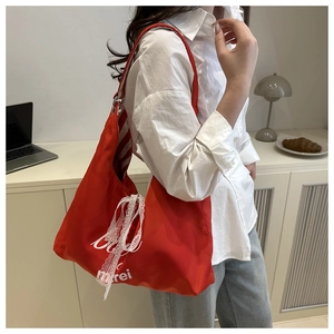 Detail of red canvas tote bag featuring white lace bow and striped lining on shoulder strap
