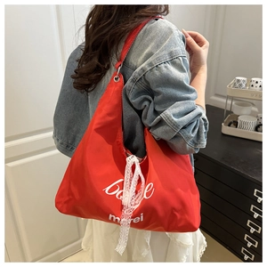 Detail of red canvas tote bag with white merci print and lace ribbon strap detail