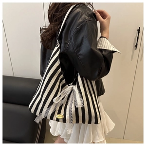 Detail of striped tote bag featuring delicate white lace bow and handmade metal plaque