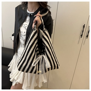 Close-up of black and white striped tote bag featuring lace bow and gold brand detail