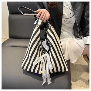 Detailed shot of striped canvas tote bag featuring a white lace bow and black handle