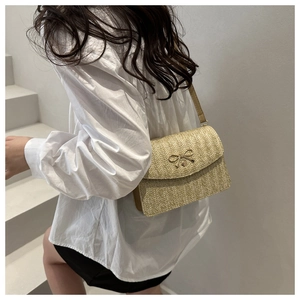 Detail of light brown woven straw crossbody bag with golden metal bow buckle on flap
