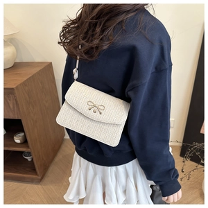Close-up of a cream woven crossbody bag with a gold butterfly buckle shown on a model